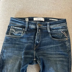 Replay Anbass slim fit jeans blå - Replay Anbass jeans i klassisk blå tvätt med slitningar och kontrastsömmar. Jeansen är i ett väldigt bra skick med noll skada! St: W28, L32. Tvättas innan den säljes. Pris kan möjligtvis diskuteras. 