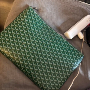 Datorfodral - Säljer en grön kuvertväska  med deras ikoniska grafiska mönster. Väskan har silverfärgad dragkedja och insida i gul textil med ett grönt innerfack. Perfekt storlek för laptop eller dokument och riktigt snygg att bära under armen.
