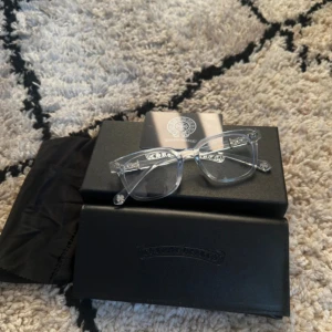 Chrome Hearts glasögon - Säljer ett par stilrena glasögon från Chrome Hearts med transparent båge och rektangulär form. Snygga silverdetaljer vid gångjärnen ger en exklusiv känsla. Kommer med originalfodral och putsduk. Perfekta för dig som vill sticka ut med en clean look. INGEN BOX MED!