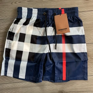  Burberry badshorts  - Snygga badshorts från Burberry i klassiskt rutigt mönster med marinblå, vita, svarta och röda detaljer. Shortsen bär storlek M men sitter som S. Perfekta för stranden eller poolen, riktigt stilren vibe.