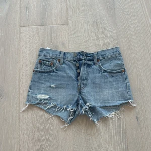 Levi's ljusblå jeansshorts W24 - Snygga ljusblå jeansshorts från Levi's med slitna detaljer och fransig kant. Klassisk femficksmodell, knappar framtill och hög midja. Perfekta för sommaren och ger en cool, avslappnad vibe.