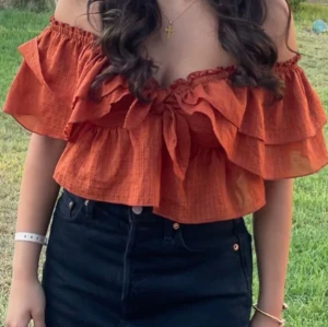 Zara topp - Superfin rostorange offshoulder topp från Zara med volanger och knyt framtill. Toppen är croppad och har ett diskret rutigt mönster i tyget. Perfekt för varma dagar när du vill sticka ut lite extra.