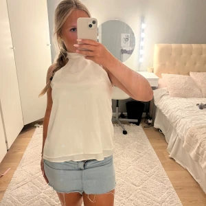 Halterneck topp - Säljer en flowy vit blus med hög hals och tunna axelband. Toppen är lätt och luftig med dubbla lager tyg som ger en snygg siluett. Perfekt till jeans eller kjol för en fräsch look. Passar dig som gillar stilrena och enkla plagg.