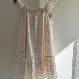 Klänning från Zara - Supersöt och populär kort klänning från Zara i ljusbeige med broderade blommor i brunt med volangdetaljer vid axelbanden och nertill. Perfekt för sommaren!!