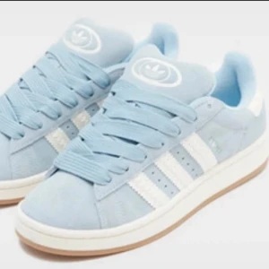 Adidas Campus ljusblå sneakers mocka - Snygga Adidas Campus sneakers i ljusblå mocka med klassiska vita ränder på sidorna och vit sula. Skorna har rund tå, platt sula och snörning. Perfekta för dig som gillar en clean och sportig stil med retrovibbar.