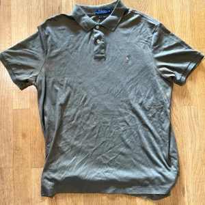 Olivgrön pikétröja Polo Ralph Lauren XL - Snygg olivgrön pikétröja från Polo Ralph Lauren i mjuk bomull. Klassisk krage, två knappar och ikoniska broderade loggan på bröstet. Perfekt för en clean och avslappnad stil. Passar dig som gillar tidlös design och premiumkänsla.
