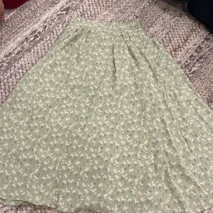 Grön blommig kjol - Supersöt kjol från Dazy i ljusgrönt med små vita och gula blommor. Kjolen har en flowy passform, diskret dragkedja i sidan och är fodrad. Storlek S