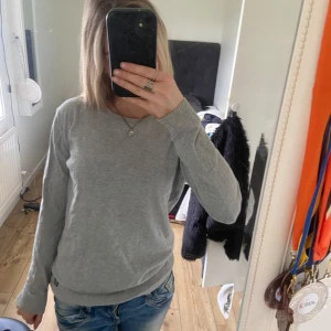 Grå stickad tröja med rund hals från H&M - En enkel och stilren grå stickad tröja med rund halsringning och långa ärmar från H&M. Perfekt för lager-på-lager och passar till både jeans och kjol. Tröjan har ribbade muddar vid ärmslut och nederkant för en snygg passform. Storlek 152/164 men sitter som en XS. 