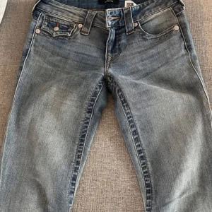True Religion ljusblå jeans - Säljer ett par snygga ljusblå jeans från True Religion med klassiska kontrastsömmar och ikoniska bakfickor med lock och knapp. Jeansen har normal passform.