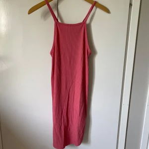 Rosa ribbad klänning med smala band - Enkel och snygg rosa gklänning med smala axelband och ribbad struktur. Klänningen har rak passform och är tillverkad i ett mjukt, stretchigt material som känns skönt mot huden. Perfekt för varma dagar när du vill ha något bekvämt men ändå stilrent.