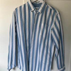 Blåvit randig skjorta från MNG Man - Snygg blåvit skjorta från MNG Man med breda vertikala ränder och klassisk krage med knappar. Skjortan har en bröstficka och är långärmad med regular fit. Perfekt för dig som gillar en stilren och fräsch look.