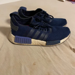 Adidas NMD sneakers marinblå - Snygga Adidas NMD sneakers i marinblå mesh med klassiska tre ränder på sidan. Skorna har vit och lila sula med coola detaljer och snörning framtill. Perfekta för dig som gillar streetstyle och bekväma skor med modern design.
