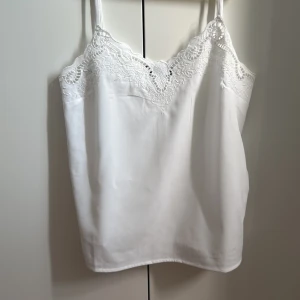 Vit linnetopp med spetsdetaljer - Säljer en vit linnetopp med tunna axelband och vacker spets längs urringningen. Supersöt och skön till sommaren. Från BURTON of London, storlek S.