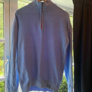 Blå stickad half zip-tröja NZA - Snygg ljusblå stickad tröja från NZA med strukturerat mönster och ribbad hög krage. Half zip-dragkedja framtill med cool detalj på dragaren. Långärmad och perfekt för lager-på-lager-stil. Badge på ena ärmen för extra vibe. Ny pris runt 2 tusen