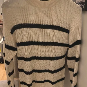 Randig stickad tröja  - Snygg stickad tröja från 157 i storlek XS. Tröjan är vit med svarta ränder och har en klassisk rund halsringning. Den är långärmad och har en loose fit, perfekt för en chill och avslappnad stil.