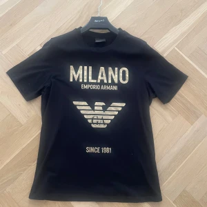 Svart Emporio Armani t-shirt med guldtryck - Svart t-shirt från Emporio Armani. Köptes för 1999kr , pris kan diskuteras vid snabb affär. Finns qr kod