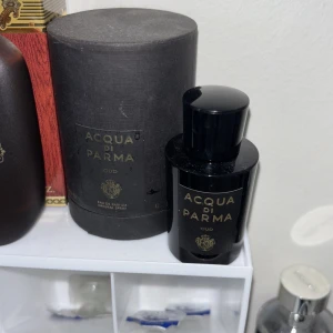 Acqua di Parma Oud Parfym (flaskan är tom)  - Lyxig parfym från Acqua di Parma i svart glasflaska med guldfärgad text och matchande svart cylinderformad förpackning. Doften är Oud, vilket ger en exklusiv och djup karaktär. Perfekt för dig som gillar eleganta och sofistikerade dofter.