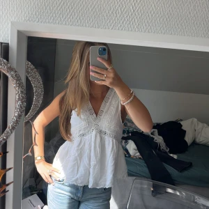Vit broderad linnetopp från Zara - Supersöt vit linnetopp från Zara med broderade detaljer och spets längs v-ringningen. Toppen är ärmlös och har en luftig, lätt utsvängd passform. Klicka gärna på ”köp nu”!
