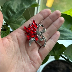 Cool vintage brosch med röda stenar - Superfin brosch i form av en blomma med gnistrande röda stenar och silverfärgade detaljer. Blomman har ett glittrigt utseende och fästs enkelt med nål på baksidan. Perfekt för att ge din outfit en extra touch av glamour.