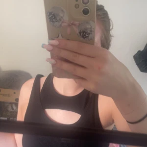 Svart ribbad linnetopp från H&M - Svart ribbad linnetopp från H&M med cool cut out-detalj vid bröstet. Toppen är ärmlös och har en tight passform som framhäver figuren. Perfekt för dig som gillar en trendig och edgy look.
