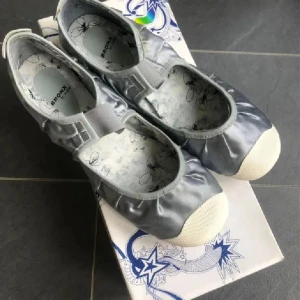Silvriga ballerinaskor från Bronx - Snygga ballerinaskor från Bronx i metallic-silver med elastiskt band över foten för extra komfort. Skorna har rund tå, vit platt sula och blommigt mönstrad innersula. Perfekta för dig som vill ha en stilren men ändå cool look. Satin/läder . På vissa ställen syns lim som kom fram , syns på bilderna 