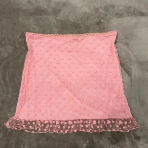 Rosa blommig kjol från Sugar Thrillz - Supersöt slutsåld rosa kortkjol från Sugar Thrillz med små 3D-blommor över hela tyget och volangkant längst ner. Kjolen har en mesh-liknande yta och är perfekt för dig som gillar gulliga detaljer och pastelliga vibes.