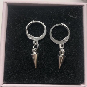 Silvriga örhängen med konformad detalj - Säljer ett par coola silvriga örhängen med små konformade hängen. De har en enkel ringdesign med en snygg, minimalistisk vibe och passar perfekt för dig som gillar edgy accessoarer.