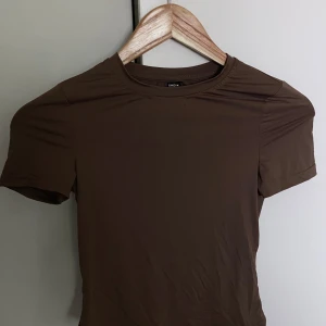 Brun kortärmad topp från SHEIN - En enkel brun topp från SHEIN med rund halsringning och korta ärmar. Modellen är figurnära och passar perfekt till jeans eller kjol för en clean look. Materialet känns mjukt och stretchigt mot huden