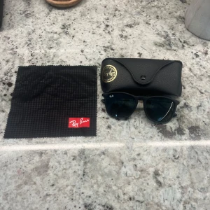 Svarta Ray-Ban Wayfarer solglasögon - Snygga svarta Ray-Ban Wayfarer solglasögon med mattsvart båge och mörka glas. Klassisk fyrkantig form, levereras med originalfodral och putsduk. Perfekta för att lyfta din stil och skydda ögonen mot solen.