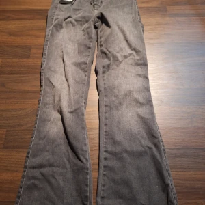 Grå bootcut jeans från FitJeans S - Snygga grå jeans från FitJeans i modellen Flared Fitjeans Shorter. De har bootcut-ben, klassisk femficksdesign och hög midja. Jeansen är gjorda i stretchigt denim som sitter skönt och ger en clean look. Perfekta för dig som gillar en modern siluett.