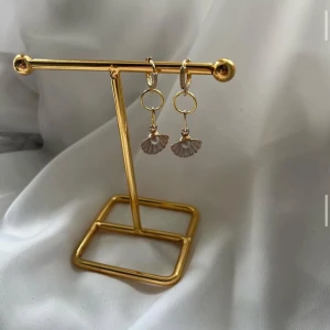 Guldiga örhängen med snäckhänge - Snygga örhängen i guld med små snäckformade hängen och en pärldetalj i mitten. Perfekta för dig som gillar unika accessoarer med havsinspiration. Hängena är eleganta och ger en cool touch till din stil.