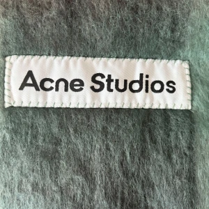 Rutig halsduk från Acne Studios - Supermjuk, lång och fluffig halsduk från Acne Studios i rutigt mönster med toner av grått, grönt och brunt. Stora rutor och långa fransar i ändarna ger en cool vibe. Perfekt accessoar för att lyfta din höst- eller vinterstil.