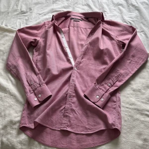 Rosa skjorta från Tiger of Sweden - Snygg rosa skjorta från Tiger of Sweden i slim fit-modell. Skjortan har klassisk krage, långa ärmar med manschett och vita knappar framtill. Perfekt för dig som gillar stilrena och moderna plagg med en fräsch färg.