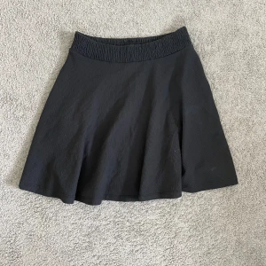 Svart lätt ribbad kjol - Svart kortkjol från 157 med bred resår i midjan som ger en skön och flexibel passform. Kjolen har en lätt utställd form och är tillverkad i ett mjukt, stretchigt tyg. Perfekt för dig som gillar enkel och stilren look.