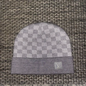 En grå tvär fet mössa med schack mönster och en logga. - Denna snygga mössan används inte därför har jag valt att sälja den. Priset kan diskuteras. Skickar oftast från 1-2 dagar.