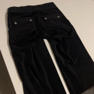 Svarta velourbyxor Juicy Couture XXS - Mysiga svarta mjukisbyxor från Juicy Couture i velour med snörning dock saknad av logga på snören. Dom har bakfickor med knappar på, klassisk broderad JC-logga på benet. Perfekta för en mjuk och trendig look.