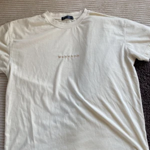 Beige t-shirt från Mennace - Säljer en stilren beige t-shirt från Mennace med diskret broderad logga på bröstet. T-shirten har normal passform och är tillverkad i mjuk bomull. Perfekt för en avslappnad och enkel look.