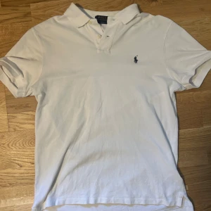 Vit pikétröja från Polo Ralph Lauren - Klassisk vit pikétröja från Polo Ralph Lauren med broderad logga på bröstet. Perfekt för den varma sommaren som kommer.