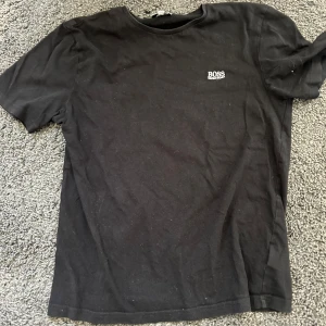 Svart t-shirt från Hugo Boss - Säljer en klassisk svart t-shirt från Hugo Boss med liten logga på bröstet. T-shirten har rund halsringning och korta ärmar. Perfekt basplagg för garderoben.