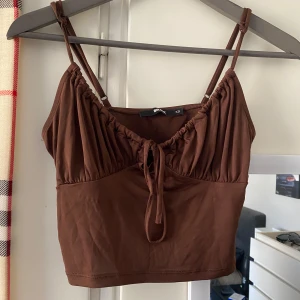 Brun linnetopp från Bik Bok - Säljer en snygg brun linnetopp från Bik Bok med smala justerbara axelband och knytning framtill. Toppen har en rynkad design vid bysten och är mycket bekväm💗🦋