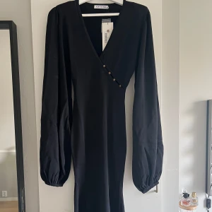 adoore klänning  - Säljer en svart långklänning från Adoore med v-ringning och dekorativa knappar framtill. Klänningen har långa puffärmar och en figur form. Klänningen är helt ny med prislapp kvar.