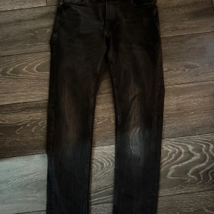 Svarta jeans från Smog/Denim - Säljer ett par svarta jeans från Smog/Denim i storlek 28/30. Jeansen har klassisk femficksdesign, raka ben och diskreta slitningar framtill för en cool look. Perfekta för dig som gillar en enkel och stilren stil.