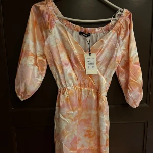 Pastellfärgad omlottklänning från bikbok  - Säljer en superfin kortklänning från bikbok i pastelliga toner av rosa, orange och vitt. Klänningen har v-ringning, omlottdesign och trekvartsärmar med resår. Perfekt för sommarens alla tillfällen!