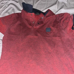 Röd piké t-shirt från BOSS - Snygg röd piké t-shirt från BOSS med klassisk krage och knappar framtill. Tillverkad i mjuk pima bomull för extra komfort. Diskret BOSS-logga på bröstet och korta ärmar. Perfekt för en stilren och avslappnad look. Äkta.