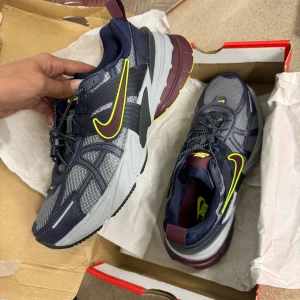 Nike sneakers i grått och svart med neongula detaljer - Säljer ett par helt nya Nike sneakers i grått och svart med neongula detaljer och vinröd sula. Skorna har meshpaneler för bra ventilation och en kraftig yttersula för extra grepp. Perfekta för dig som vill ha en sportig och modern look. 