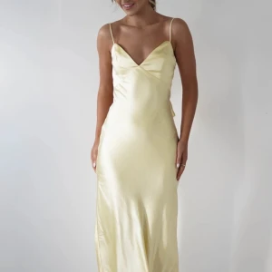 Balklänning  - Säljer en ljusgul långklänning i satin med smala axelband, v-ringning och öppen rygg med knyt i midjan. Klänningen har en elegant och enkel siluett som faller snyggt längs kroppen. Aldrig använd endast testad.💕💕💕