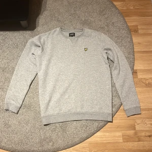 Grå sweatshirt från Lyle & Scott Junior - Säljer en stilren grå sweatshirt från Lyle & Scott Junior med rund halsringning och klassisk gul logga på bröstet. Perfekt basictröja med normal passform och mjukt material som passar till det mesta.