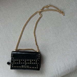 Svart axelväska med guldkedja från Ideal of Sweden - Snygg svart axelväska från Ideal of Sweden med guldfärgade nitar och kedja. Liten och smidig modell💛