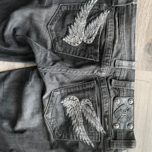 Miss Me jeans bootcut flare W27 emo goth - Snygga svarta jeans från Miss Me med unika broderade vingar på bakfickorna. Jeansen har en bootcut-stil och är dekorerade med metallknappar och detaljer. Perfekta för dig som vill ha något extra i garderoben.