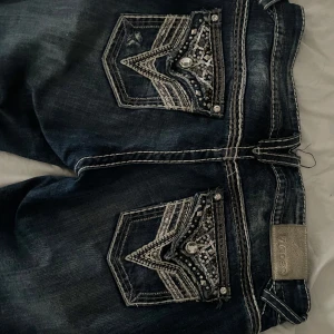 Mörkblå bootcut jeans med bakfickor från Vigoss - Säljer ett par mörkblå jeans från Vigoss med snygga broderade och dekorerade bakfickor med pärlor och nitar. Jeansen har kontrastsömmar och klassisk femficksdesign. Jag älskar dom här jeansen men dom är lite för korta på mig som är 178cm💔
